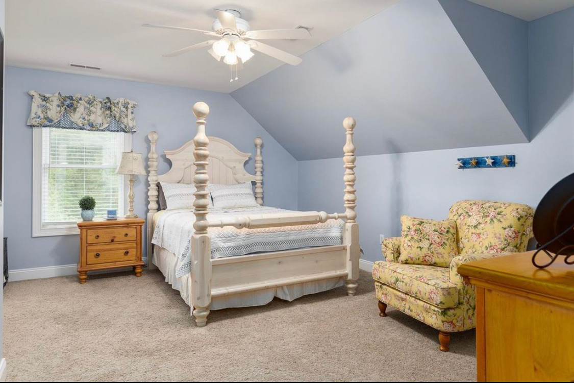 Blue bedroom with carved four-poster bed, floral chair and dormer ceiling