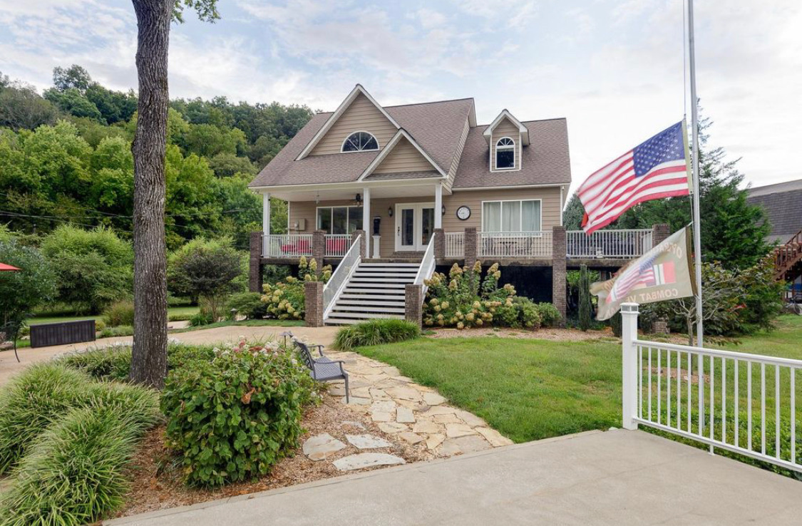 House #1 exterior with covered porch, American flag and landscaped walkway