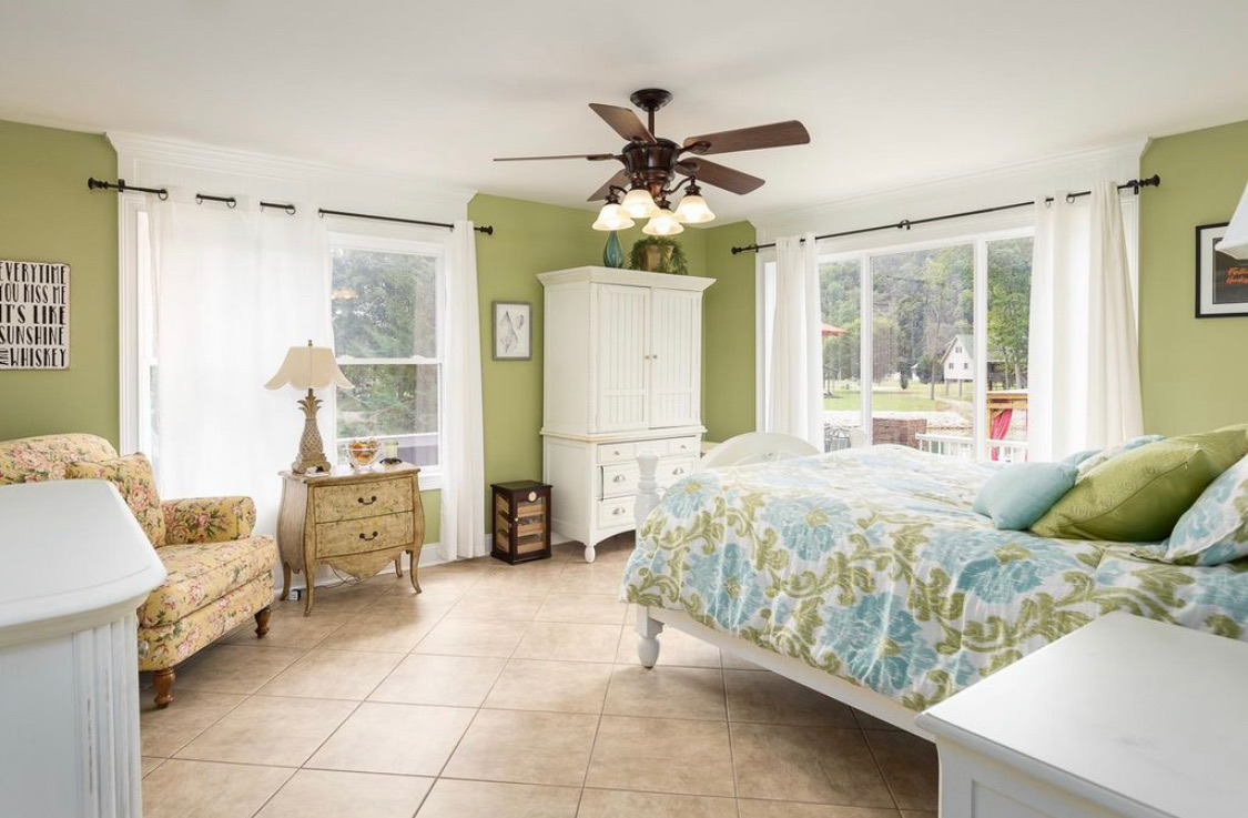 Green bedroom with white furniture, sitting chair and lake-view windows