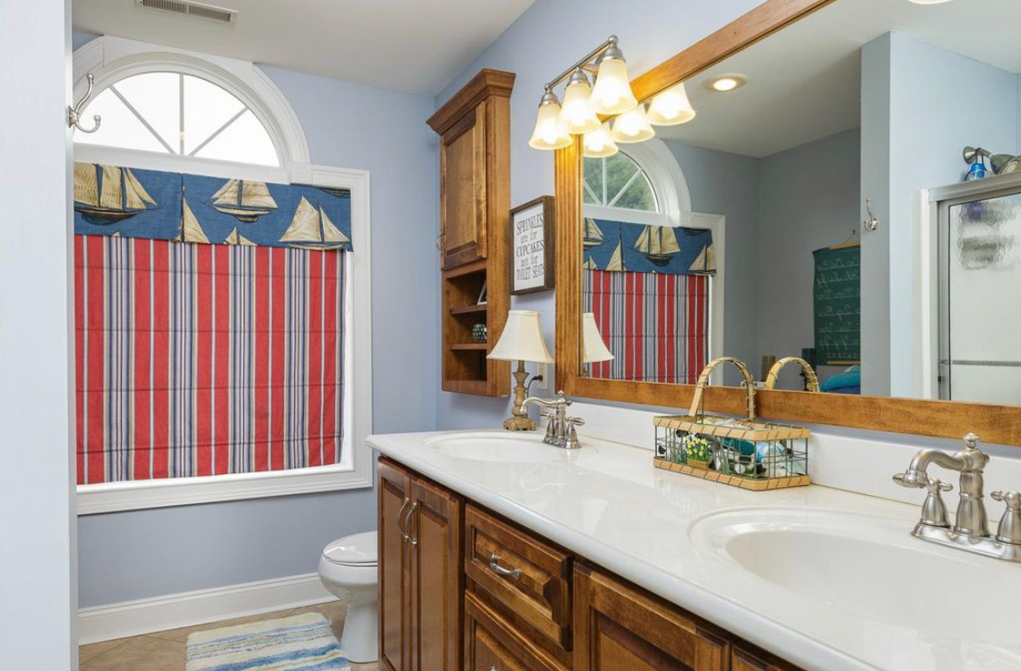 Blue bathroom with double vanity, wood cabinets and sailboat curtain