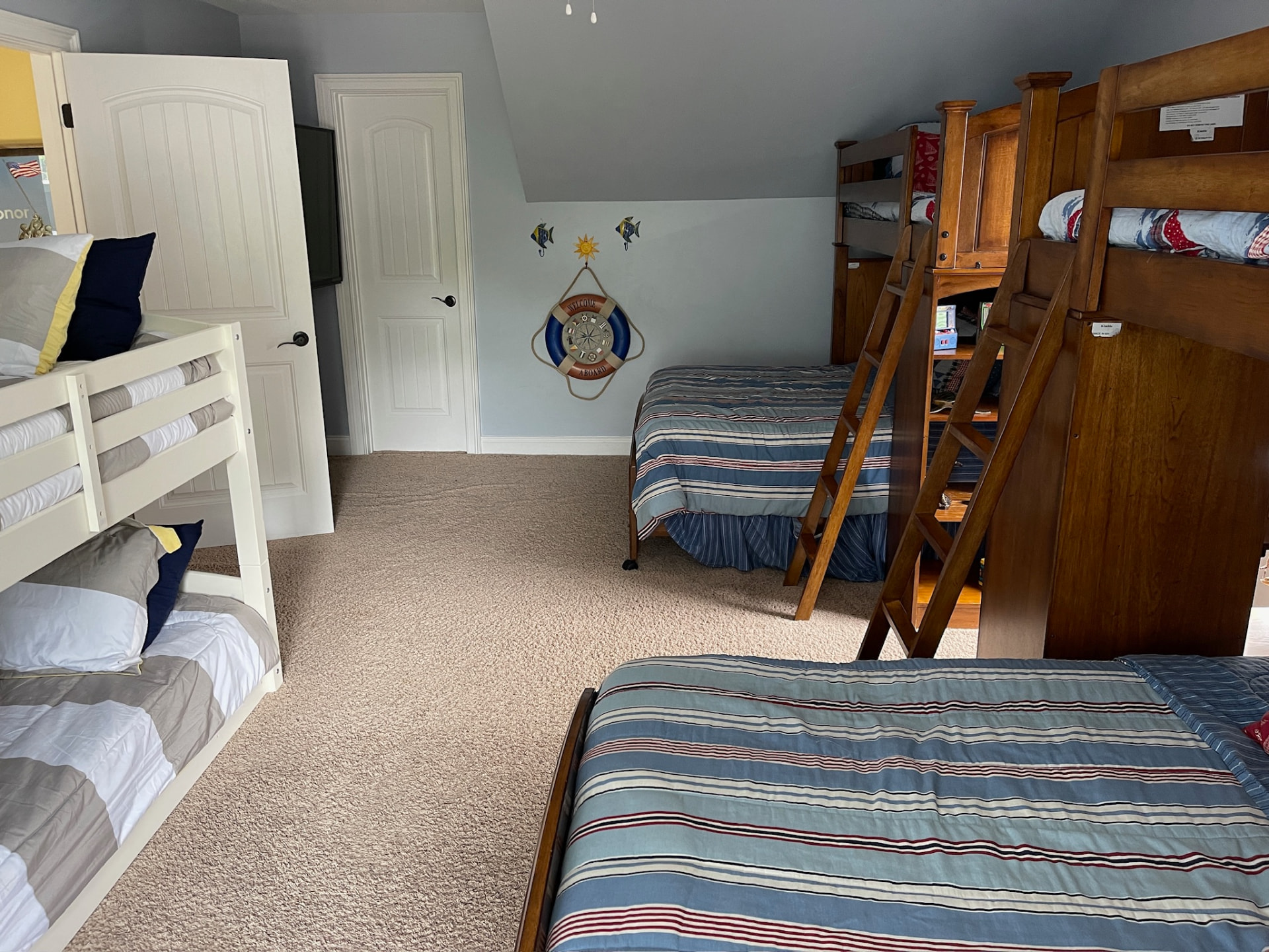 Wide bunk room with white and wooden bunks, extra beds and nautical decor